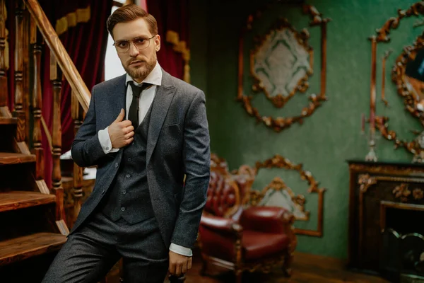 Handsome gentleman poses in a tweed suit and glasses in a vintage interior. Luxurious lifestyle. Vintage style.