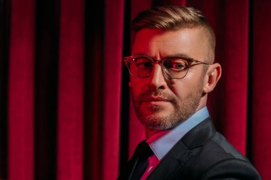 Klasik iç mekanda kırmızı ışıkta poz veren, resmi kıyafetli, olgun bir adamın yakın plan portresi. Erkek güzelliği, moda.