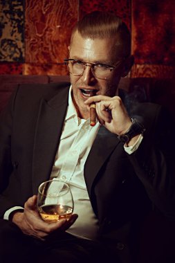 Pahalı takım elbiseli, gözlüklü, viski içen ve lüks bir dairede puro içen orta yaşlı yakışıklı bir adamın portresi. Başarı ve zengin yaşam tarzı.