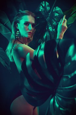 Islak saçlı güzel ateşli kadın tropikal bitkilerin arasında duruyor. Güzellik, moda ve kozmetik konsepti. Tropikal ülkelerde tatil.