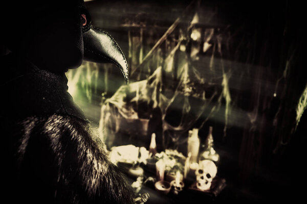 The plague doctor stands against the background of a mystical interior with skulls.Historical reenactment. Halloween. 