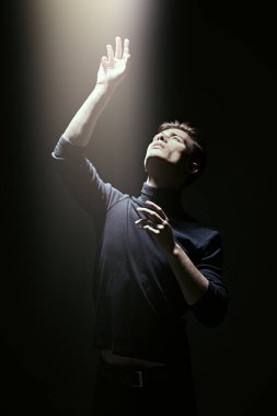 Karanlıkta duran ışığa bakan yakışıklı bir gencin sanat portresi. Siyah arkaplan.