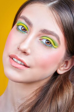 Makyaj ve makyaj malzemeleri. Sarı arka planda parlak renkli makyajlı, gülümseyen güzel bir kızın yakın plan portresi..