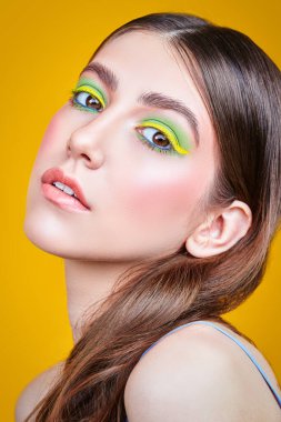 Makyaj ve makyaj malzemeleri. Sarı arka planda parlak renkli makyajlı, gülümseyen güzel bir kızın yakın plan portresi..