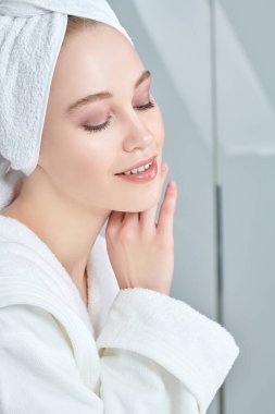 Beyaz bornozlu güzel bir genç kadın portresi ve duş aldıktan sonra saçının etrafına bir havlu. Güzellik, vücut bakımı, kaplıca.
