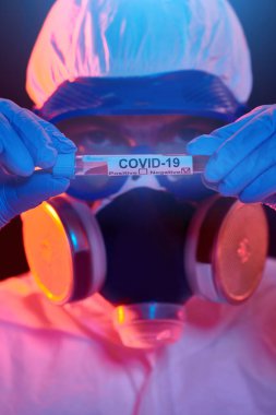 COVID-19 veya 2019-NCoV. Korunaklı PPE kıyafetli bir bilim adamının portresi. Koronavirüs test tüpünü gösteriyor. Aşılama.