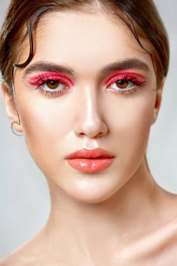 Makyaj ve kozmetik konsepti. Parlak makyajlı ve gözlerinde kırmızı oklar olan güzel bir kızın portresi. Güzellik, moda.