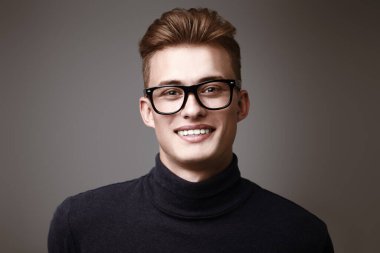 Erkek güzeli. Sarı saçlı, gözlüklü ve kameraya gülümseyen yakışıklı bir gencin portresi. Erkekler için optik.