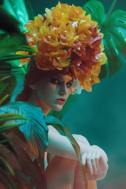 Güzel bir orkide başlığıyla tropikal bitkiler arasında poz veren modaya uygun bir kadın modeli. Güzellik ve moda konsepti. Tropik tatil.