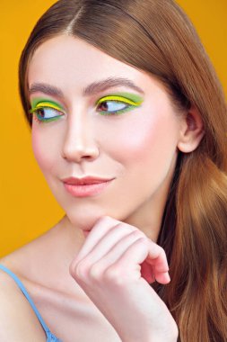 Makyaj ve makyaj malzemeleri. Sarı arka planda parlak renkli makyajlı, gülümseyen güzel bir kızın yakın plan portresi. Boşluğu kopyala.