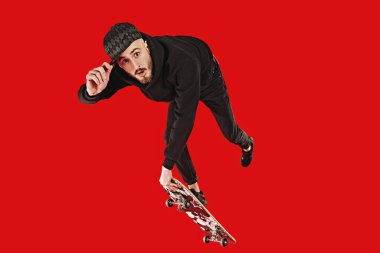 Havalı genç adam kaykayla kayıyor ve numaralar yapıyor. Aktif yaşam tarzı. Kırmızı arkaplanda stüdyo portresi.