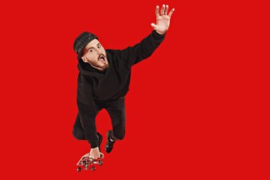 Havalı genç adam kaykayla kayıyor ve numaralar yapıyor. Aktif yaşam tarzı. Kırmızı arkaplanda stüdyo portresi.