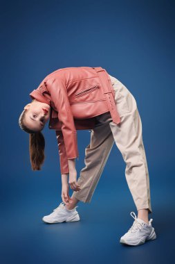 Yeni bahar stili. Koyu mavi arka planda pantolon ve deri ceketle poz veren sevimli, modern bir kız modelin portresi. Güzellik, moda. 