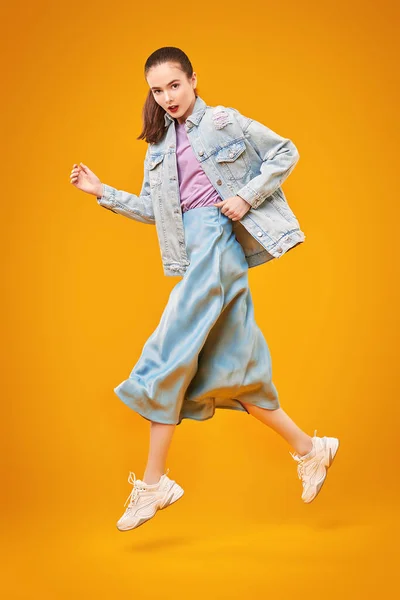 Fashion model in jeans clothes posing at studio in motion on a yellow background. Fashion, new summer style.