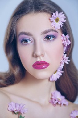 Güzel esmer bir kızın portresi. Yüzünde ve beyaz bir arka planda kasımpatı çiçekleri var. Güzellik, kaplıca ve kozmetik konsepti. 