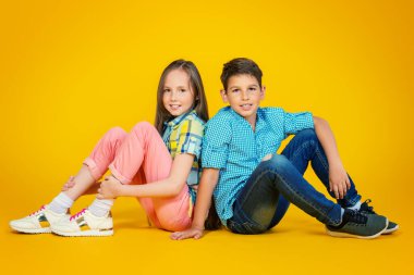 Sarı arka planda iki neşeli çocuğun uzun bir portresi. Yazlık çocuk modası. Boşluğu kopyala.