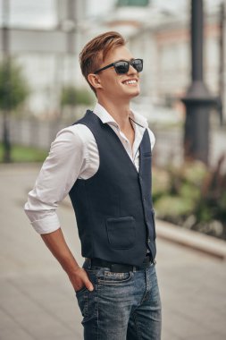Yakışıklı genç adam şehirde geziniyor ve gülümsüyor. Yaz modası. Yaz tatili ve tatil.