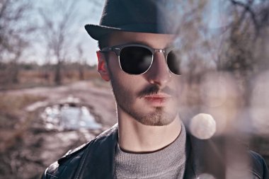 Siyah deri ceketli, güneş gözlüklü, açık havada ağaçta oturan yakışıklı bir genç. Özgürlük ve macera ruhu. Erkek modası. 