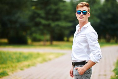 Yakışıklı genç adam parkta yürüyor ve gülümsüyor. Yaz modası. Yaz tatili ve tatil.