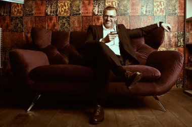 Saygıdeğer orta yaşlı bir adamın portresi günlük kıyafetler ve gözlüklerle lüks bir dairede kırmızı şarap içen. Başarı ve zengin yaşam tarzı.