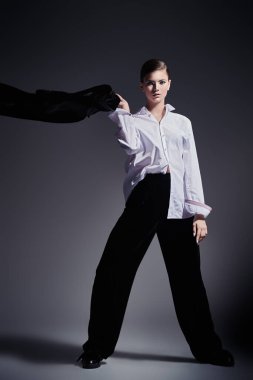 Moda konsepti. Siyah kadife takım elbise ve gri arka planda beyaz gömlekle hareket eden zarif genç bir kadının tam boy portresi.. 