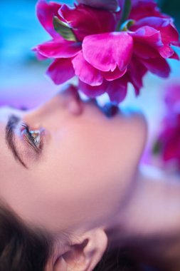 Güzellik ve çiçekler. Şakayık çiçeklerin arasında uzanan parlak makyajlı güzel esmer bir kadının yakın plan portresi. Makyaj malzemeleri, makyaj malzemeleri. Parfüm.