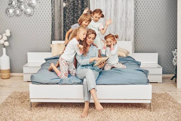 A mother reads a book to children before bed in the bedroom. Happy family at home.