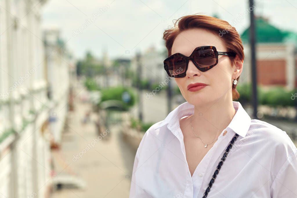 Portrait of a modern middle-aged woman in sunglasses on a city street on a summer day. Optics for women. Summer style. 