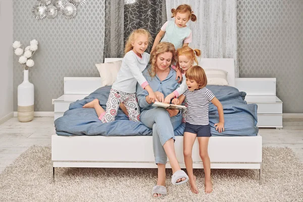 A mother reads a book to children before bed in the bedroom. Happy family at home.