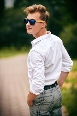 Yakışıklı genç adam parkta yürüyor ve gülümsüyor. Yaz modası. Yaz tatili ve tatil.