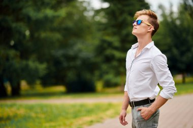 Yakışıklı genç adam şehir güvertesinde gökyüzüne doğru bakıyor. Yaz modası. Yaz tatili ve tatil.