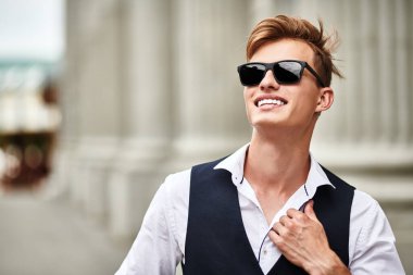 Şehirde gezinen ve gülümseyen yakışıklı bir gencin portresi. Yaz modası. Yaz tatili ve tatil.