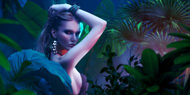 Islak saçlı güzel ateşli kadın tropikal bitkilerin arasında duruyor. Güzellik, moda ve kozmetik konsepti. Tropikal ülkelerde tatil.