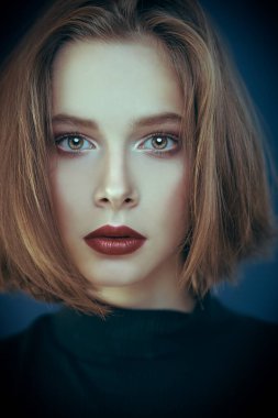 Güzellik ve kozmetik konsepti. Zarif makyajlı ve orta boy saç tıraşlı güzel bir genç kadının portresi. Koyu mavi arkaplan.