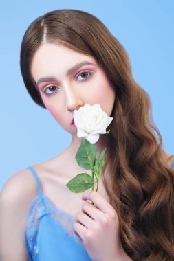 Bahar güzeli. Mavi arka planda parlak makyajlı ve açık renkli genç bir kadının portresi. Makyaj ve makyaj malzemeleri. Boşluğu kopyala.