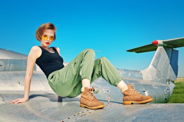 Güzel kız pilot havaalanında bir savaş uçağının kanadında oturuyor.. 