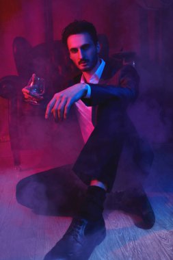 Lüks bir dairede elinde şarap kadehiyle duran yakışıklı bir esmer adamın portresi. Göz kamaştırıcı bir yaşam tarzı. Moda fotoğrafı. Erkek kıyafetleri ve aksesuarları..