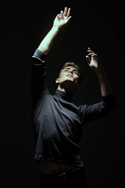 Karanlıkta duran ışığa bakan yakışıklı bir gencin sanat portresi. Siyah arkaplan.