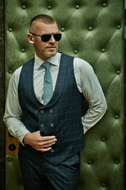 Lüks bir dairede duran şık takım elbiseli, olgun, yakışıklı bir adamın portresi. Erkek güzeli, moda. Optik, erkekler için güneş gözlüğü..