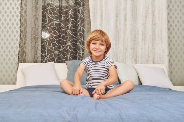 Yatakta oturmuş kameraya gülümseyen neşeli komik çocuk. Mutlu bir çocukluk. Aile evde..