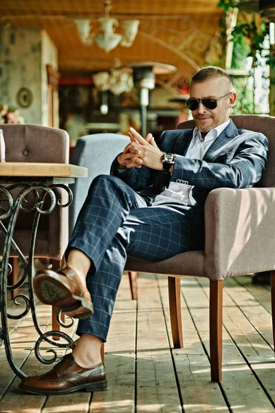 Handsome mature man in an elegant classic suit having a rest on the summer terrace. Male fashion. Optics, sunglasses for men. Summer vacation.
