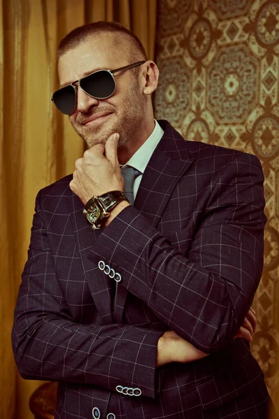 Portrait of a smiling wealthy mature man in an elegant suit and modern sunglasses in a luxury apartment. Male beauty, fashion. Optics, sunglasses for men.