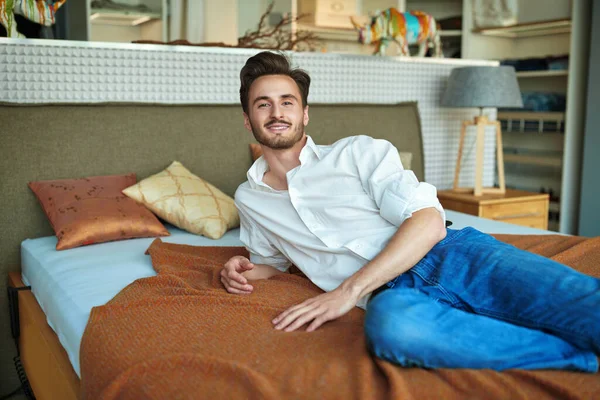 Yakışıklı genç adam evdeki yatak odasında yatağın üzerinde dinleniyor. Evin içi, mobilyalar.. 