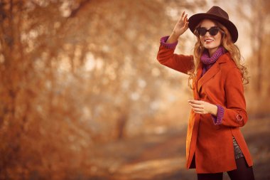 Güzel genç bir kadın sonbahar parkında yürüyor ve gülümsüyor. Sonbahar güzelliği, moda.