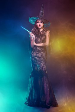 Elinde sihirli değnek tutan şapkalı güzel bir cadının portresi. Cadılar Bayramı. Kutlama.