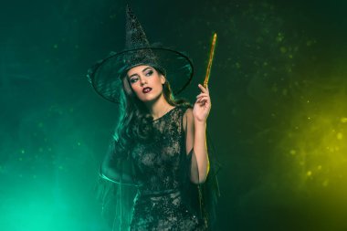 Elinde sihirli değnek tutan şapkalı güzel bir cadının portresi. Cadılar Bayramı. Kutlama.