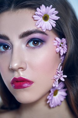 Güzel esmer bir kızın portresi. Yüzünde ve beyaz bir arka planda kasımpatı çiçekleri var. Güzellik, kaplıca ve kozmetik konsepti. 