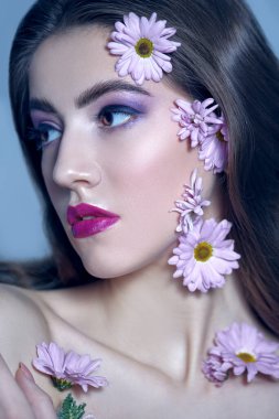 Güzel esmer bir kızın portresi. Yüzünde ve beyaz bir arka planda kasımpatı çiçekleri var. Güzellik, kaplıca ve kozmetik konsepti. 