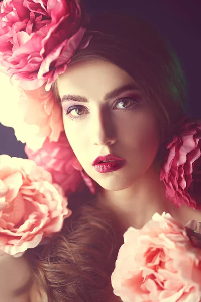 Beautiful fashion model with peony flowers in her hair on a blue background with light haze. Fashion and flowers. Make-up and hairstyle. Studio portrait.