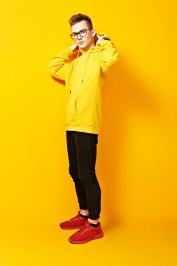 Sarı kapüşonlu ve sarı arka planda poz veren havalı genç adam. Gençlik modası.